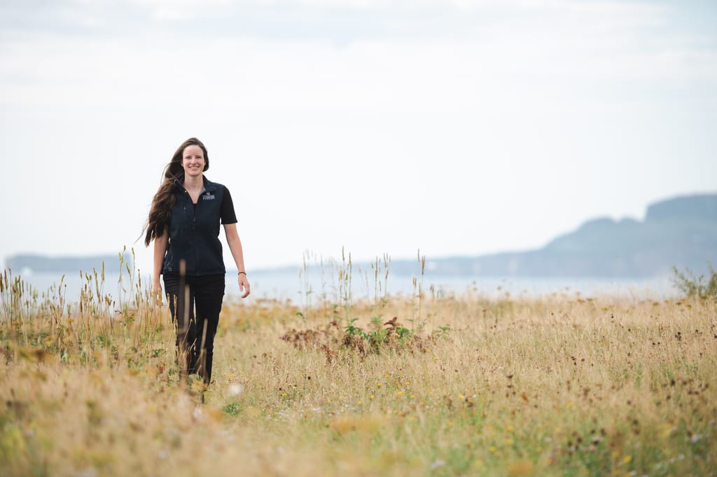 A NCC staff member walks through a field of tall grass near the coast.