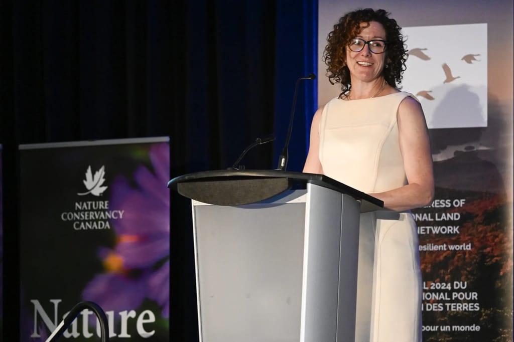 A woman in a white dress stands at a podium during an event.