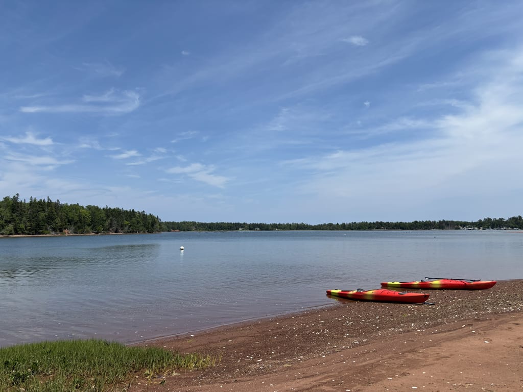 Two red kayaks sit on a reddish sandy shore by a calm lake.