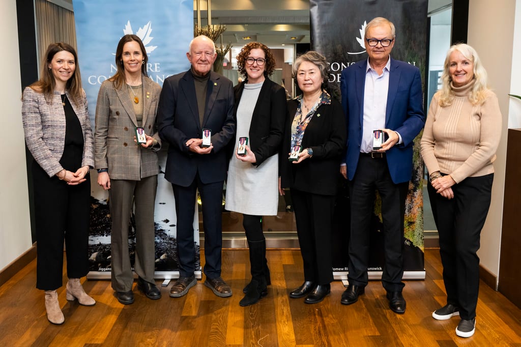 Seven people pose indoors, some holding small awards.