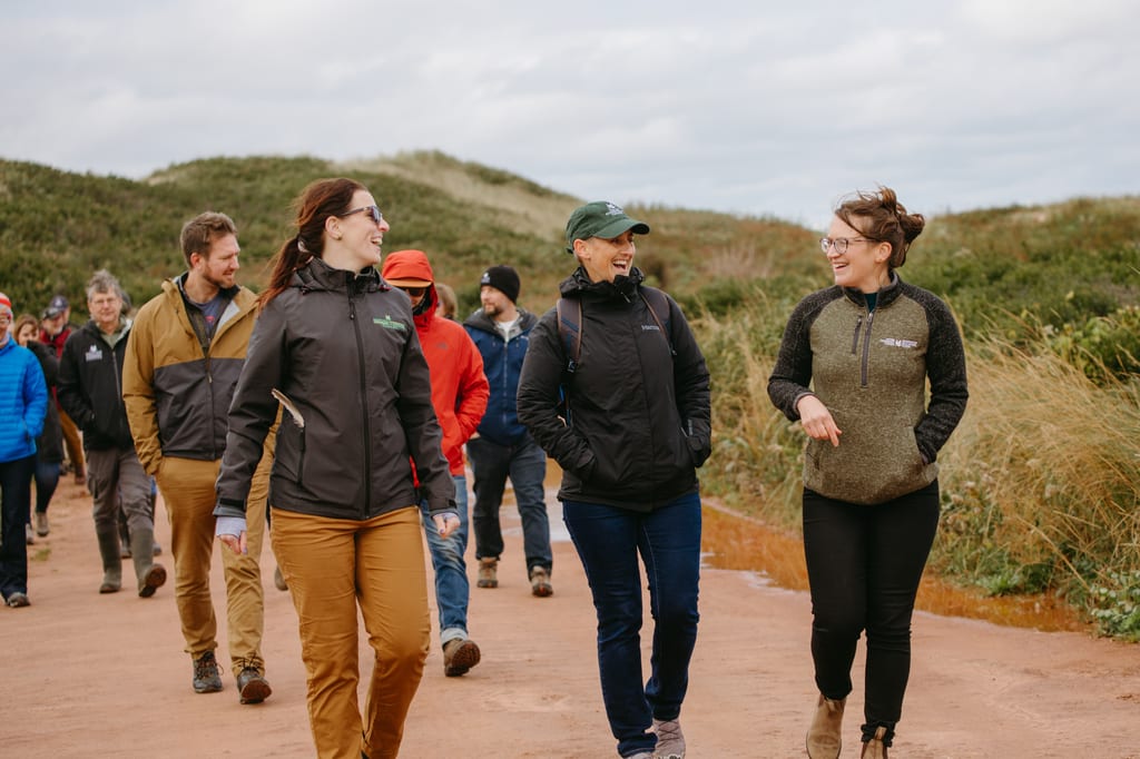 A group of NCC staff members walking along a dirt path through grassy dunes.
