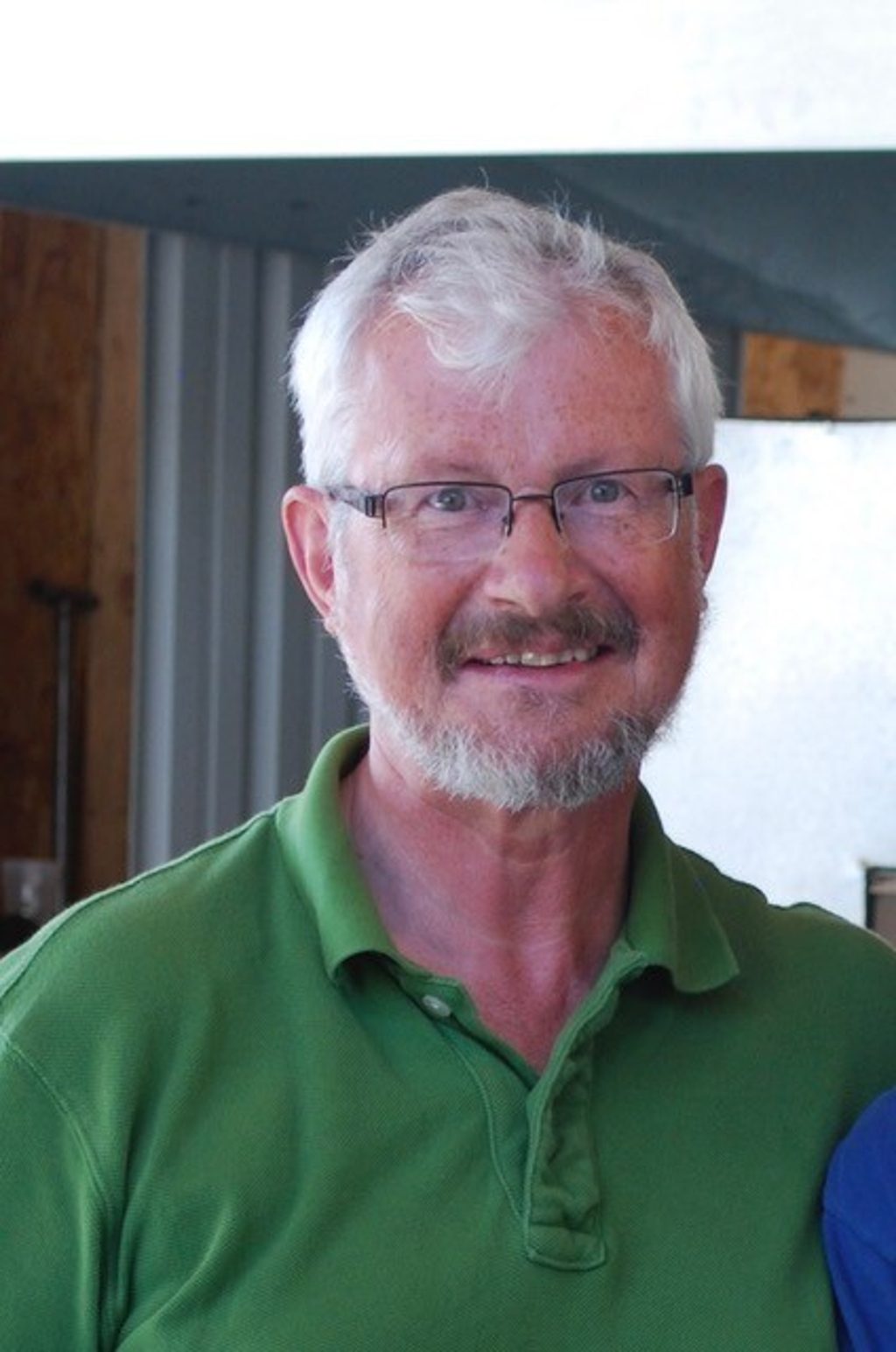 A smiling man with white hair and glasses wearing a green polo shirt.