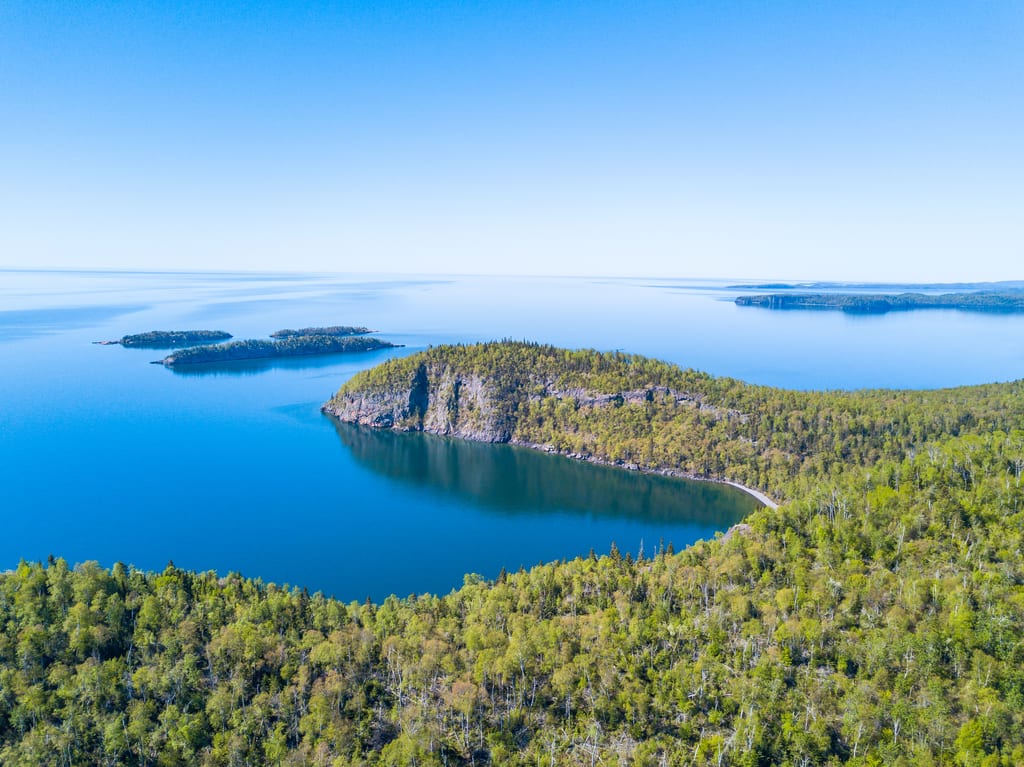 An aerial view of forested islands in a large blue body of water under a clear sky.