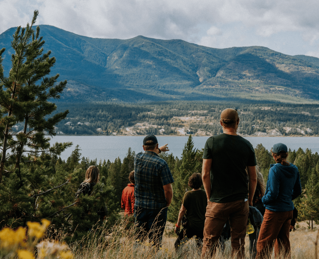 A group of people stands on a hill overlooking a lake and mountains.