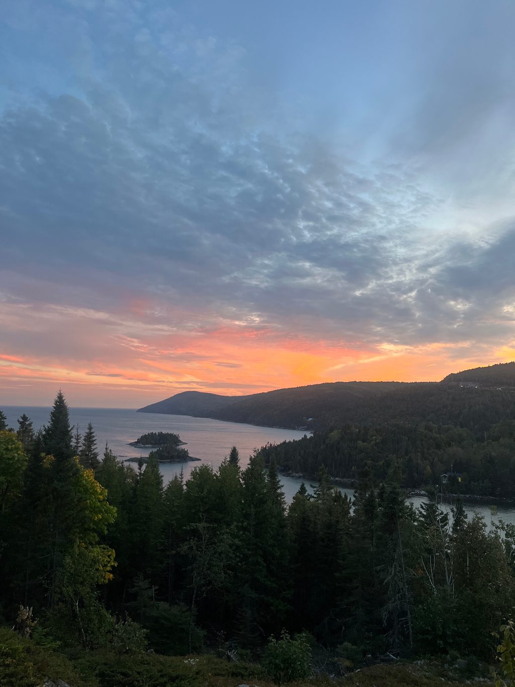 A sunset over a forested coastline with a small island in the water.