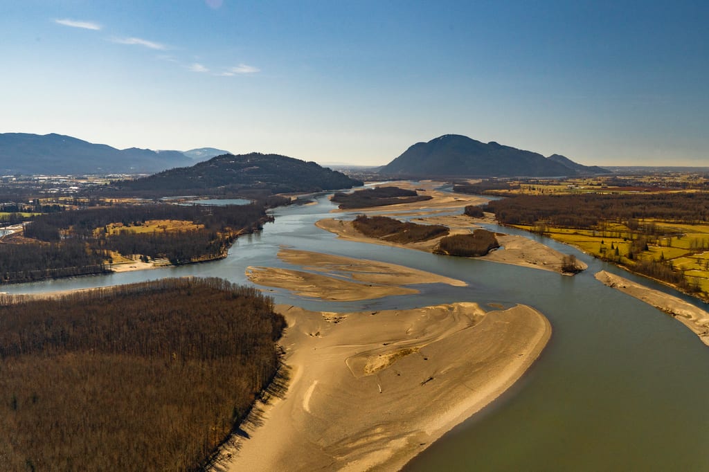 A wide river winds through a valley with sandbars and forested banks under a clear sky.