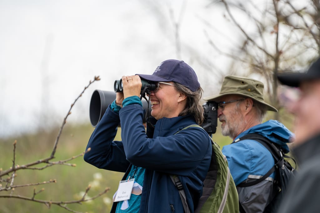 A woman uses binoculars to observe nature in a field during spring.