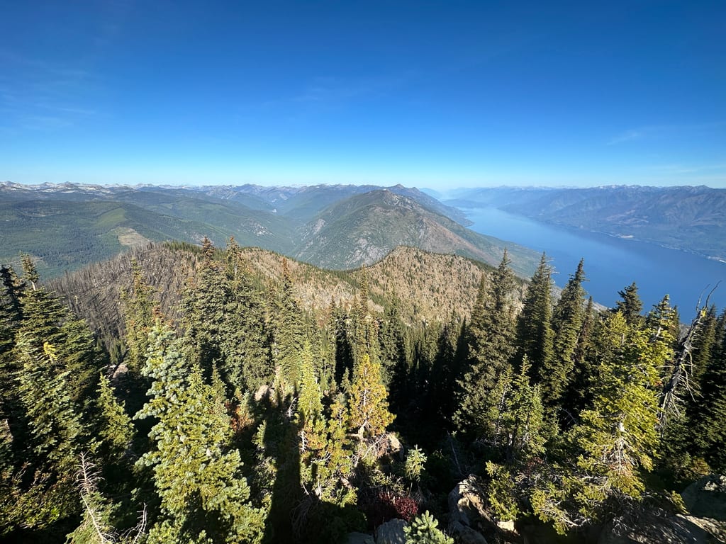A wide view of forested mountains and a large lake under a clear blue sky.