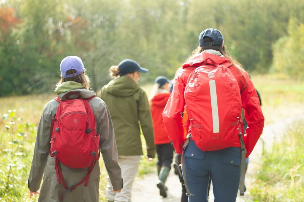 A group of people with backpacks hiking on a trail through a wooded area.