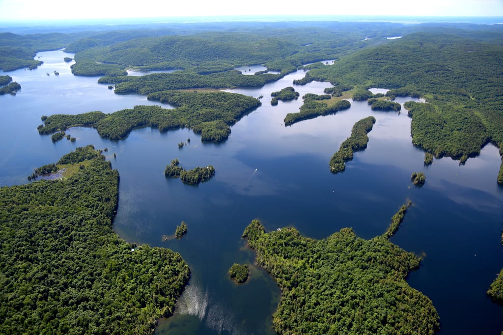 An aerial view of a large lake surrounded by dense green forests and numerous islands.