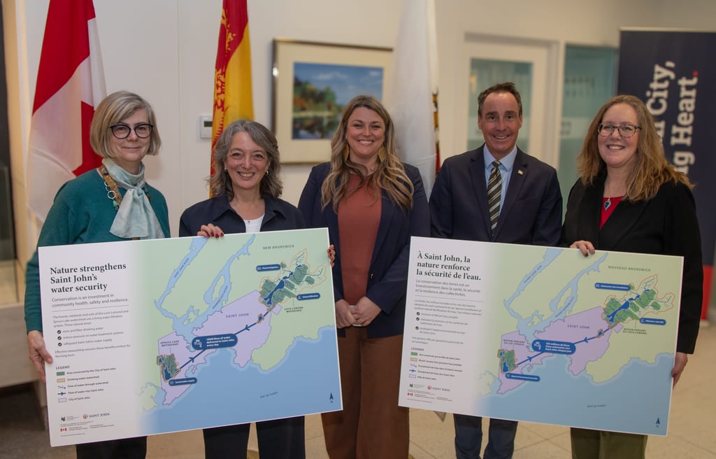 Five people stand indoors holding two large maps about water security.