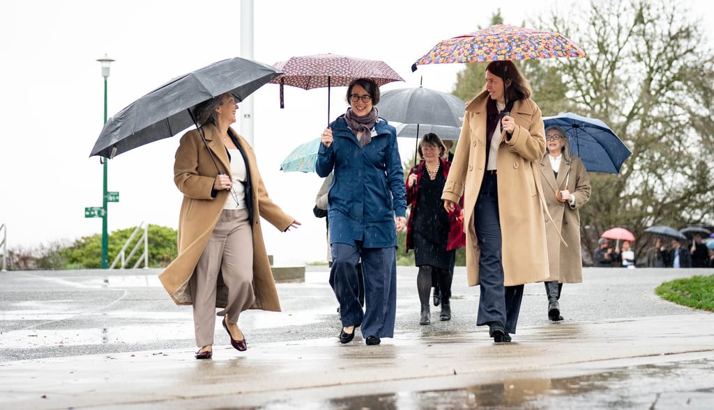 A group of people walk with umbrellas on a wet paved path during a rainy day.