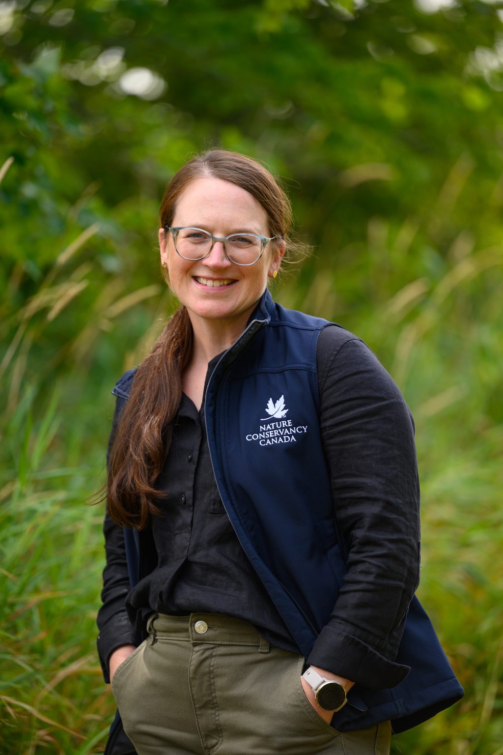 A woman wearing a Nature Conservancy Canada vest stands in a field of tall grass.