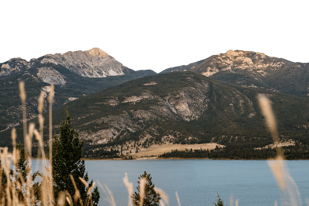 Rugged mountains rise above a forested slope and a calm lake.