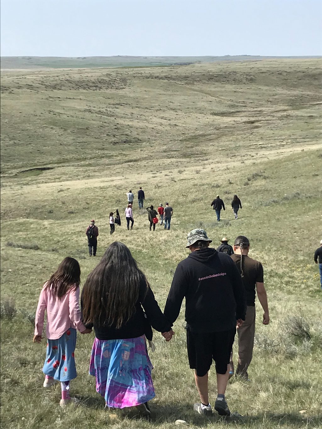 A group of people hiking through a vast, rolling grassland landscape.