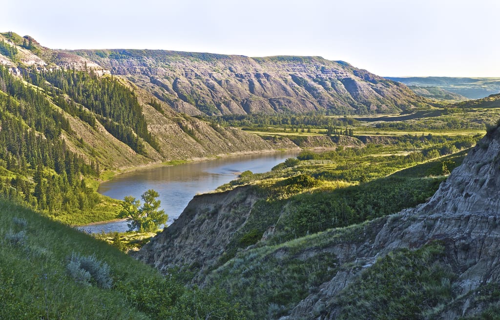 A scenic view of a lake surrounded by forested hills, rocky cliffs and mountains.