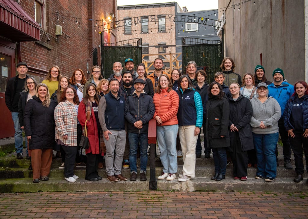 A large group of people posing for a photo in an urban alleyway between brick buildings.