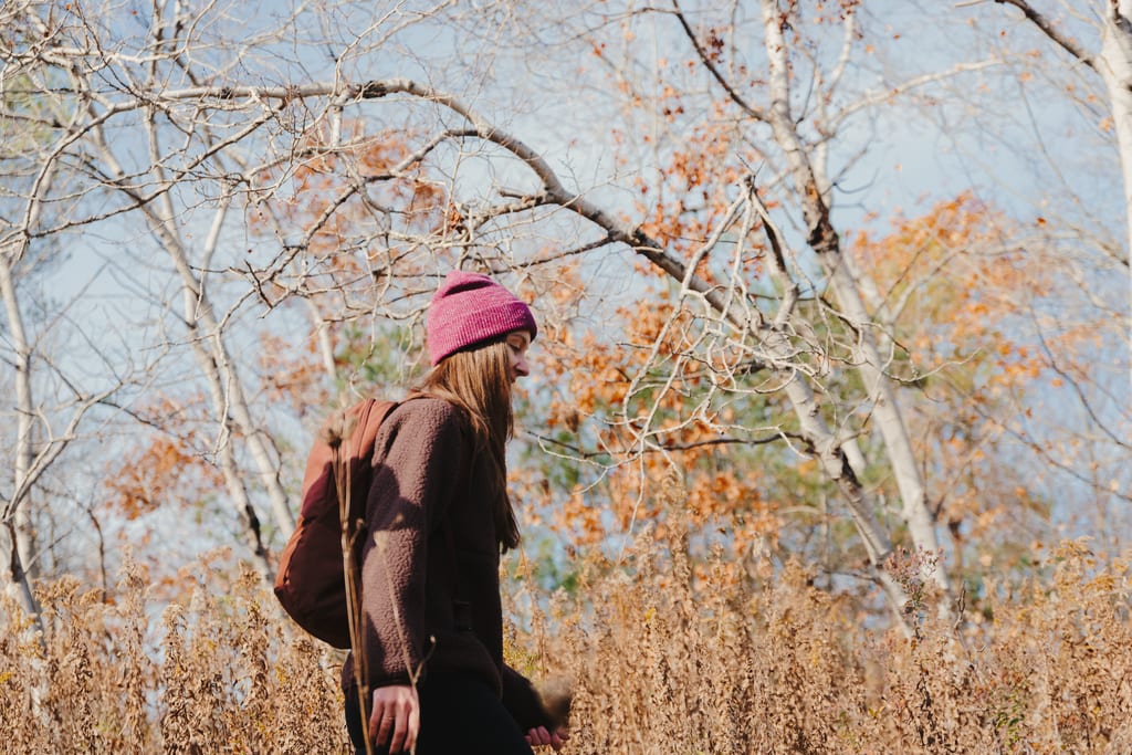 A person wearing a pink beanie and a backpack walks through a field of tall, dried grass.