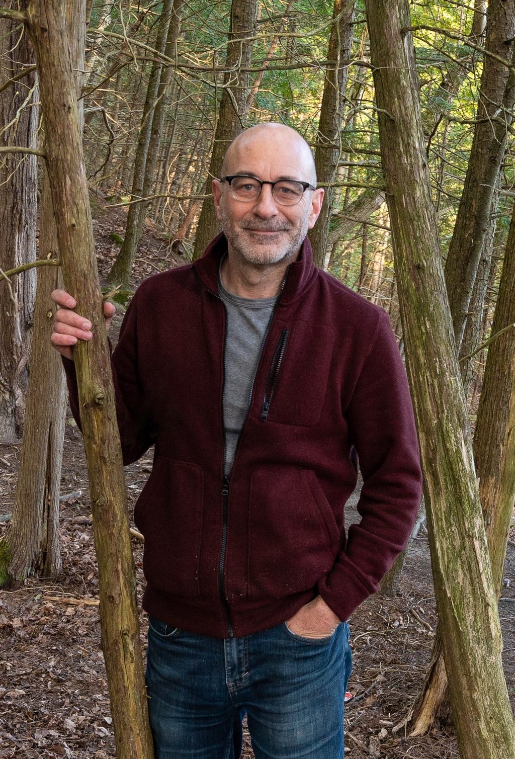 A man in a maroon jacket stands in a forest.