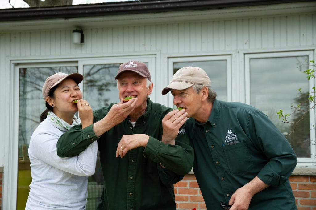 Three people are eating green snacks in front of a white building.
