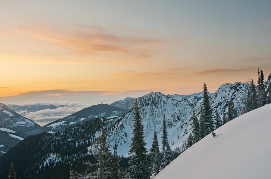 Snow-covered mountains and evergreen trees under a sunset sky.