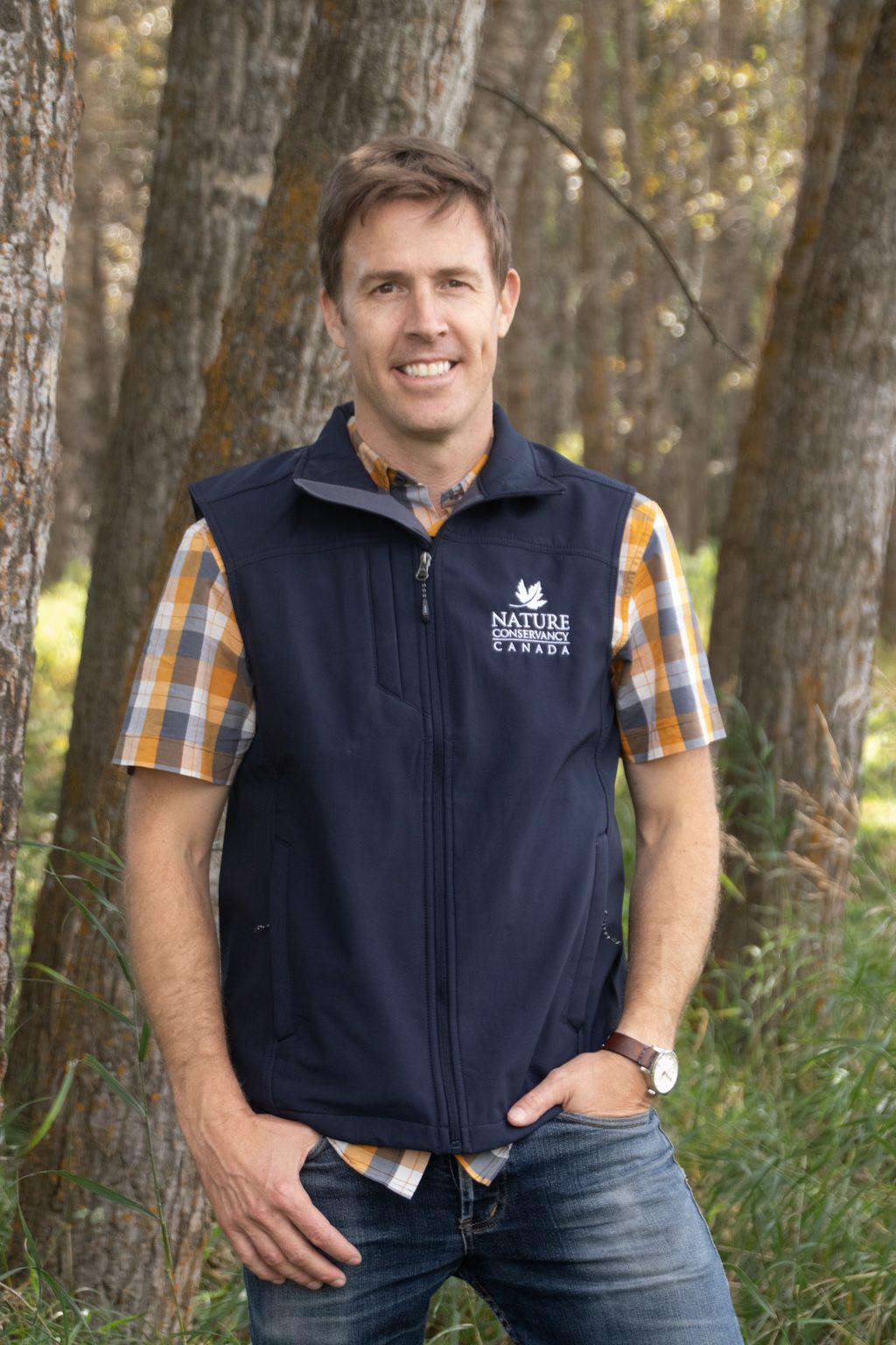 A man wearing a Nature Conservancy Canada vest stands in a forest.