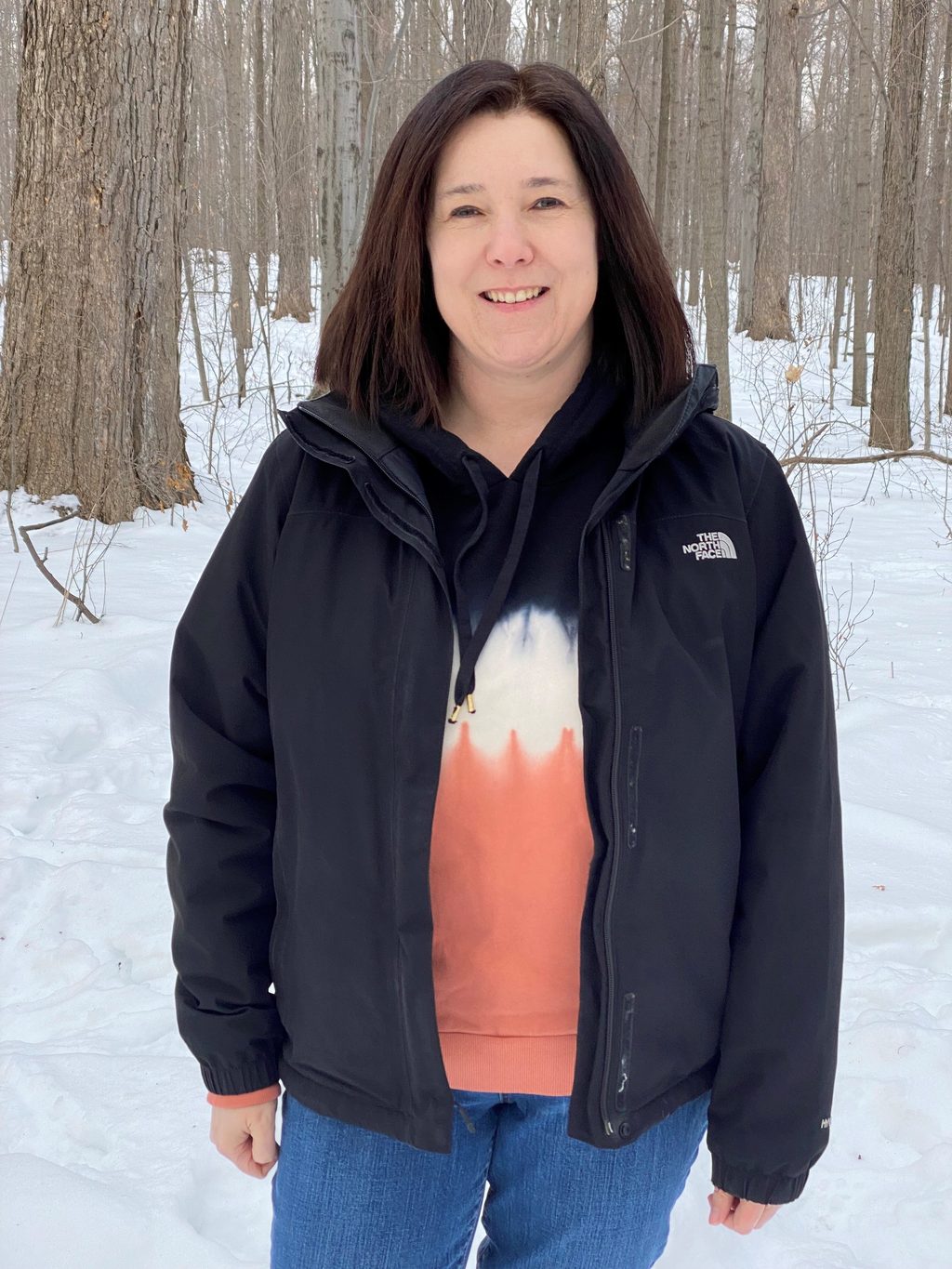 A woman stands in a snowy forest.