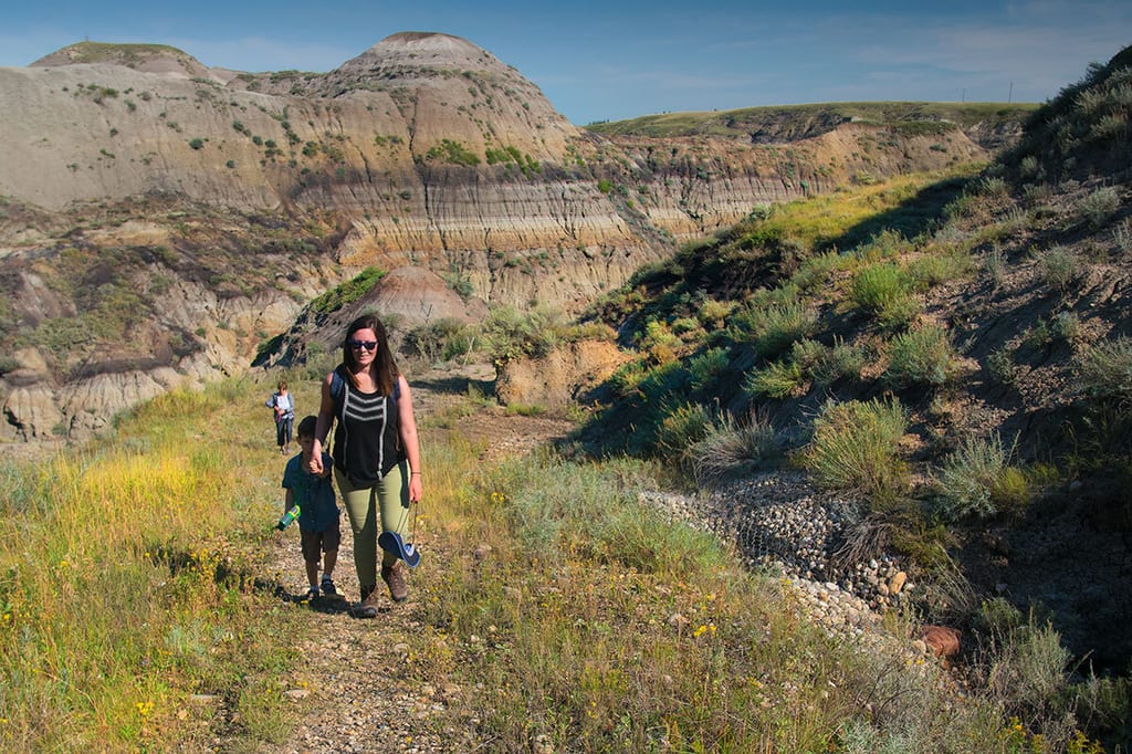 A woman and two children walk along a trail through a badlands landscape with eroded hills.